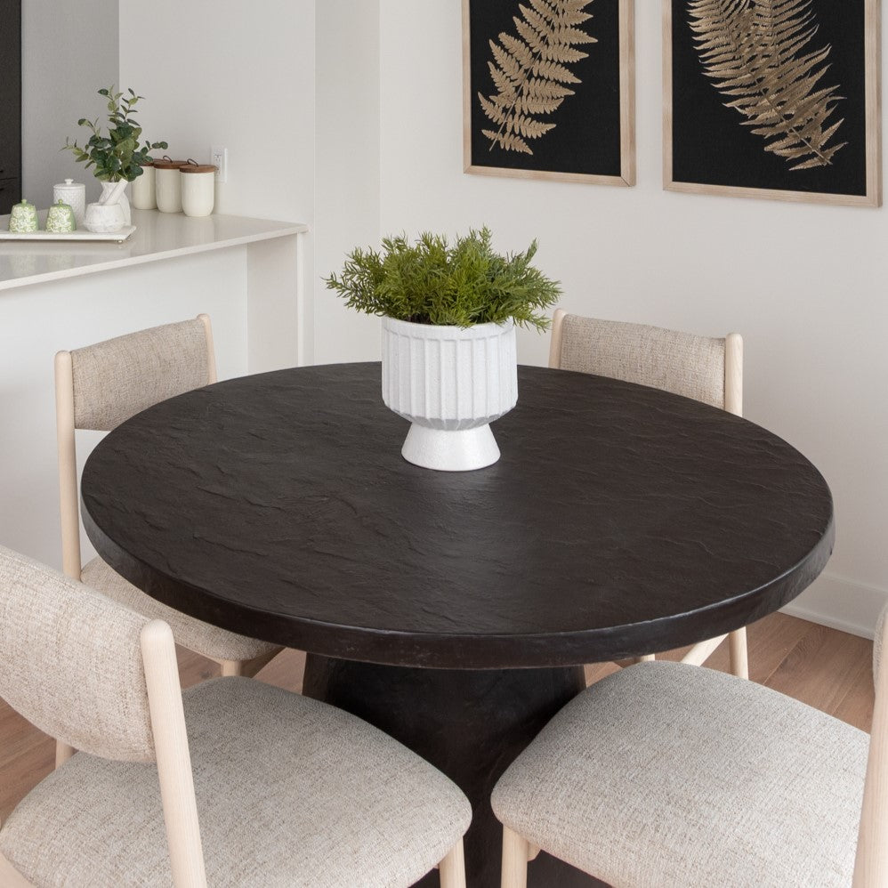 Round black wooden contemporary dining table with light contrast modern dining chairs. Styled with white vase full of greenery and leaf nature inspired wall art