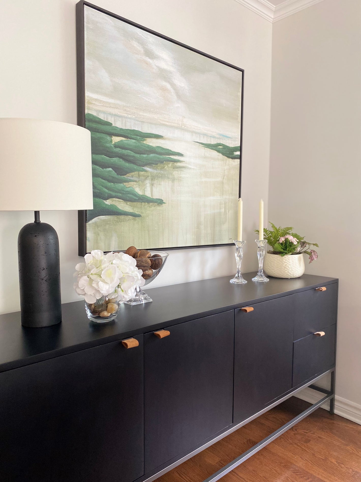 Modern black console table with decorative items against a wall with nature inspired framed artwork.