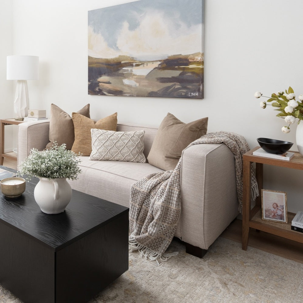 Cozy living room with beige sofa, decorative pillows, and a painting on the wall. Warm modern home style