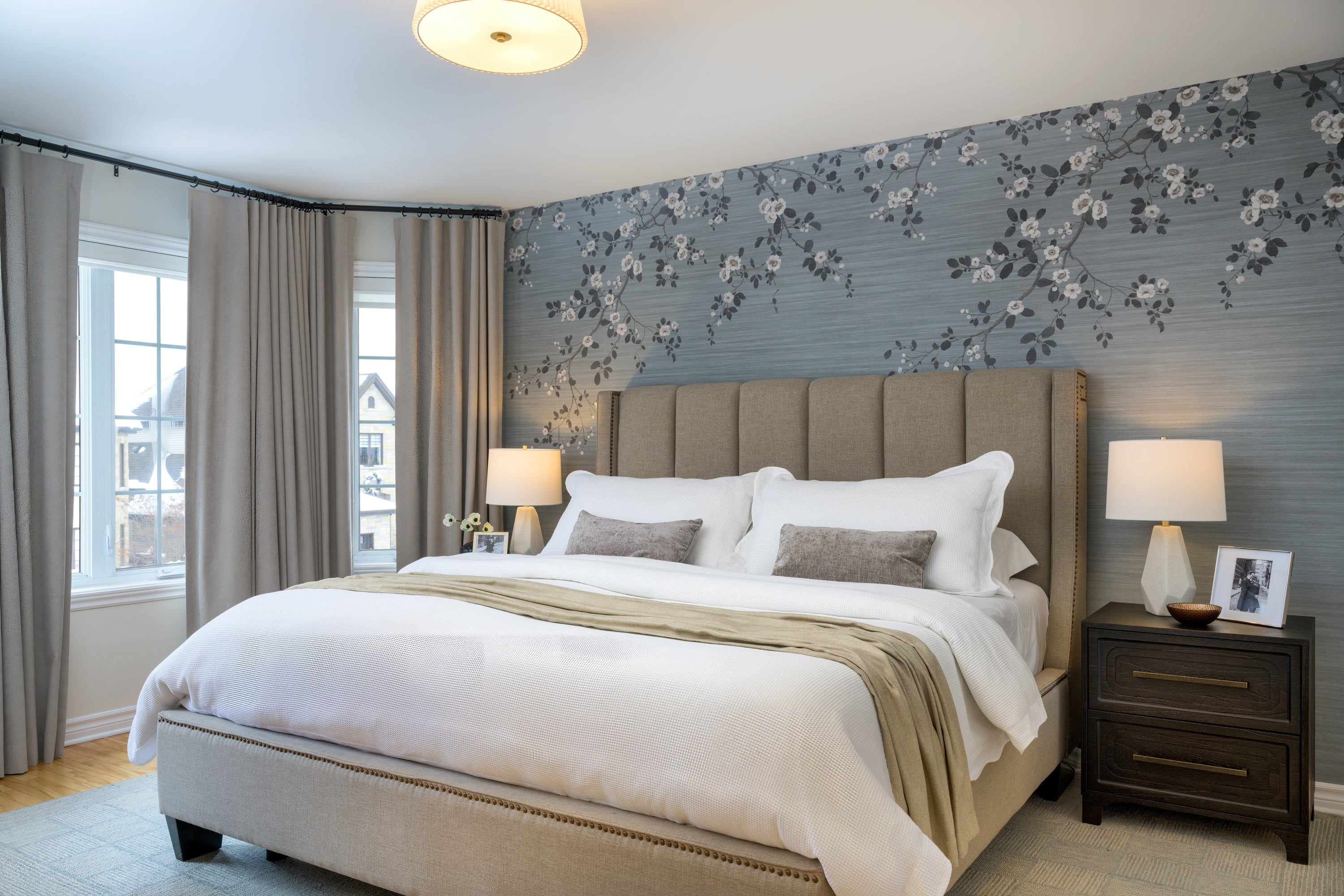 Beige upholstered bed with channel headboard in traditional style bedroom with two drawer nightstands and elegant floral wallpaper wall mural.